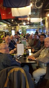 Group of people dining at a long table in a decorated restaurant with flags and photographs.