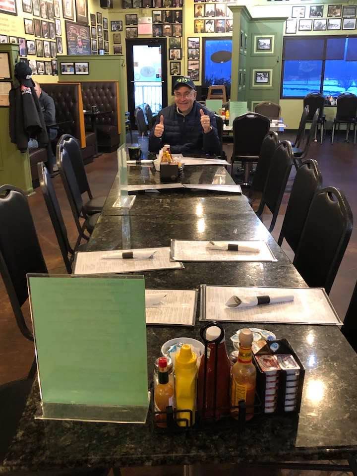 Person giving thumbs up at a long table in an empty restaurant with framed photos on walls.
